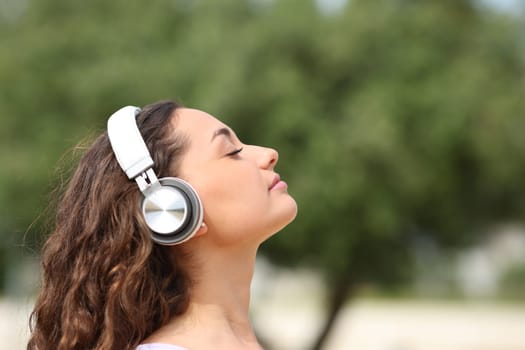 Profile of a relaxed woman with headphones meditating in a park