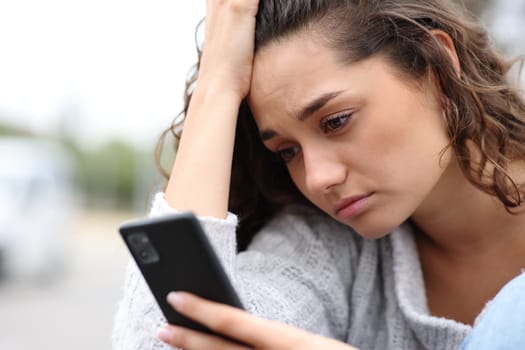 Sad woman checking phone message complaining in the street