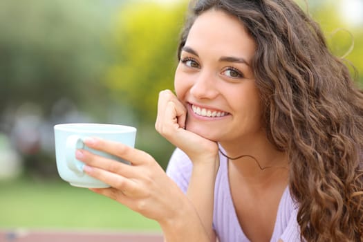 Happy woman holding coffee cup posing in a park