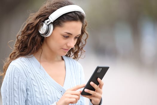 Woman wearing headphones checks phone outdoors in the street