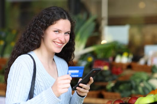 Woman buying online in a greengrocery with phone and credit card