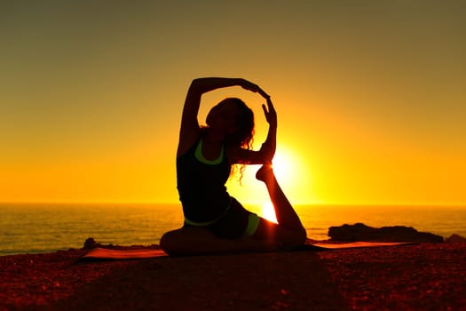 Silhouette of a yogi doing yoga advanced exercise at sunset on the beach