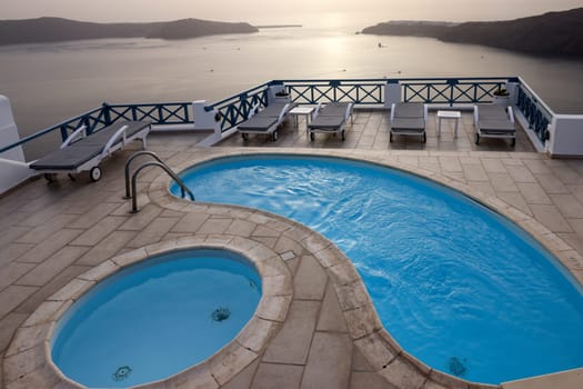 Sun loungers and pools on terrace in the village of Imerovigli with amazing view of sunset over caldera in Santorini. Greece