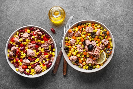 Healthy tuna salads mixed with corn, peppers, carrot, peas and beans on grey background. Mexican corn salad.