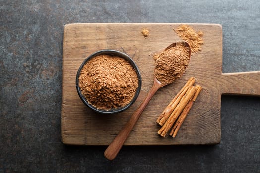 Aromatic cinnamon sticks with cup and spoon with powder on grey background close up