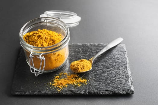 Curry powder (turmeric) in glass jar close up. Indian mixture of finely ground spices