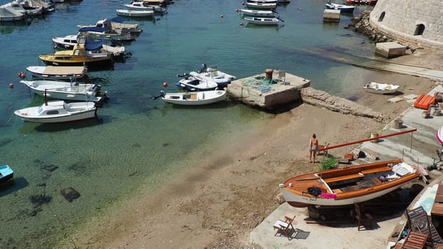 Dubrovnik, Croatia, August 14, 2022. City port in summer, tourist attraction. Tourists walk, get into boats and ships and go on boat trips. Adriatic Sea. A local resident plays with a dog. Old forts