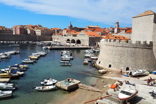 Dubrovnik, Croatia, August 14, 2022. City port in summer, tourist attraction. Tourists walk, get into boats and ships and go on boat trips. Adriatic Sea. A local resident plays with a dog. Old forts