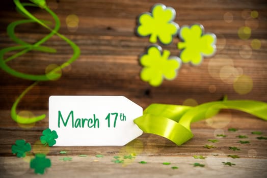 White Label With English Text March 17th. Saint Patrick's Day Decoration With Green Shamrock And Clover. Wooden Vintage Background With Festive Ribbon.