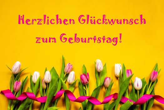 German Text Herzlichen Glueckwunsch Zum Geburtstag Means Happy Birthday. White And Pink Tulip Spring Flowers With Ribbon. Yellow Wooden Background