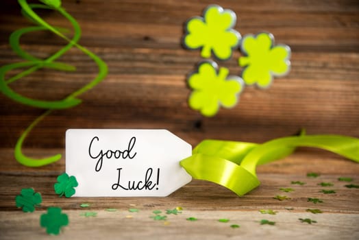 White Label With English Text Good Luck. Saint Patrick's Day Decoration With Green Clover And Shamrock. Wooden Vintage Background With Festive Ribbon.