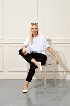 Joyful woman in black trousers and white shirt on transparent chair