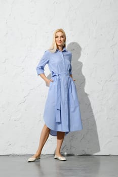 Joyful blonde woman in blue shirt dress posing