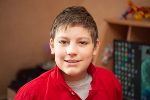 Close portrait of a smiling European teenage boy in a red shirt in his room