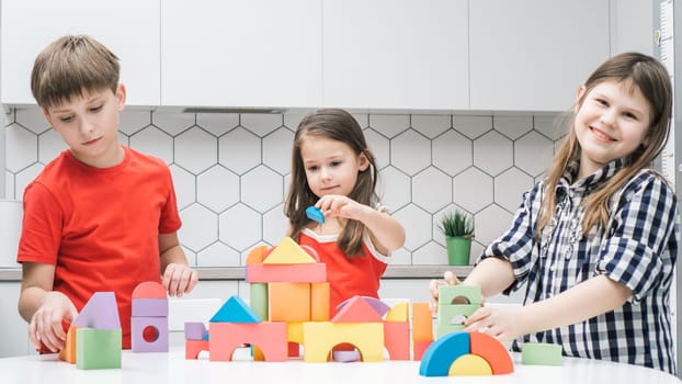 Happy school friends play toy constructor on kitchen table. Children collect colorful details of lego. Little kids build toy city. Home leisure, playtime. Educational interesting board game.
