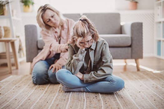 Mother taking pity on her daughter sitting on the floor. Concept of the family relation.