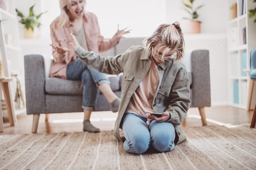 Mother arguing with her daughter chatting on smartphone. Concept of the family relation.