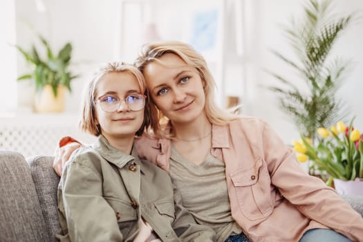 Mother and daughter sitting on the sofa indoor and embracing. Concept of the mother's day and motherhood.