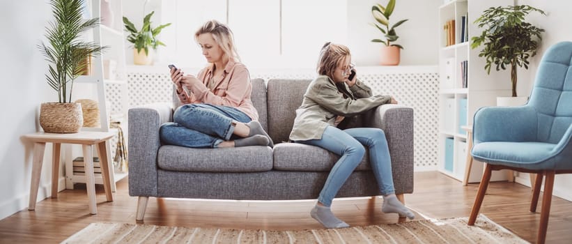 Quarreled mother and daughter sitting on the sofa back to back. Concept of the family relation.