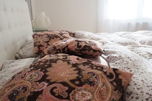 Pink decorative pillows on the bed linen. Double bridal bed with pillows and thick feather duvet. Bedroom design. Soft white headboard. Interior with furniture and bedding