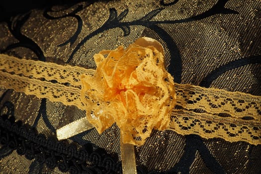 A beautiful yellow-orange lace artificial flower sewn onto a decorative cushion satin fabric. Blue dense braid with thin polyester lace. Decoration of decorative pillowcases. Women's needlework.