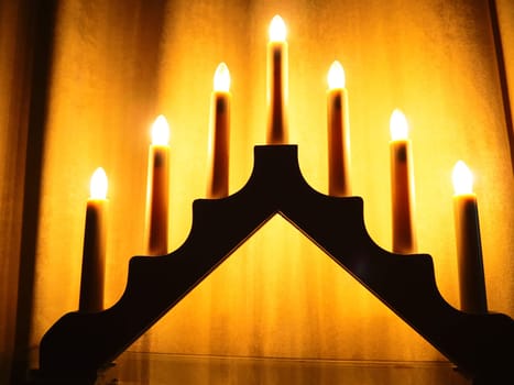 Schwibbogen arch luminaire in the form of a triangular candlestick. Yellow background. Evening, romantic, festive, religious or mystical atmosphere. Burning light bulbs that resemble candlelight.