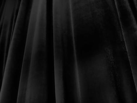 Soft waves on black velvet curtains. Stylized defocused image. Dark draperies made of pleasant fabric. Pleats on the curtains. Abstract black and gray background