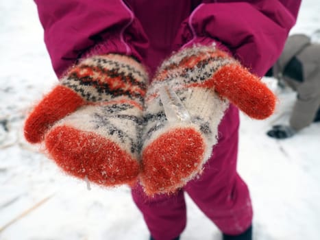 ice on mittens or gloves. Children's hands hold a frozen straw in their palms. Red knitted winter mittens stained with snow. The winter vacation. Christmas fun. Winter time in the afternoon.