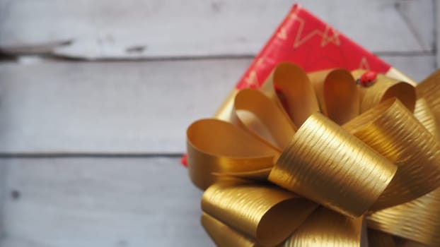 Red gift box with a large gold bow on a wooden background painted with white paint. Gift for Christmas, New Year, Birthday, Mother's Day, Wedding, Valentine's Day. Beautiful festive decoration.