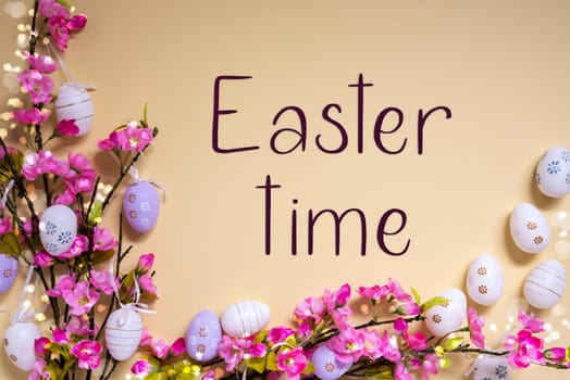 English Text Easter Time On Beige Background. Pink And Purple, Shiny And Bright Spring Flower Arrangement With Easter Egg Decoration.