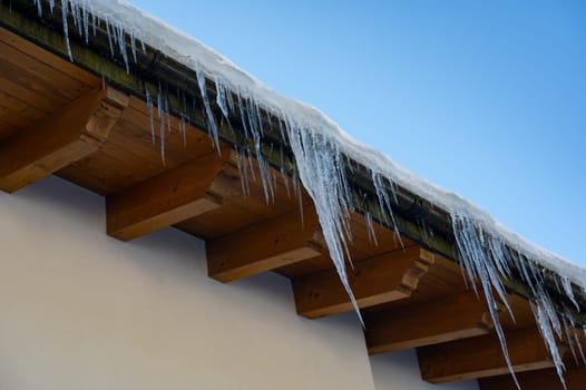 Icicles on a roof with wood and blue sky