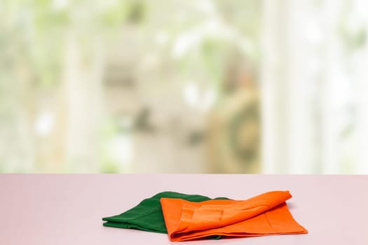 Empty table product. Closeup of a empty orange and green tablecloth or napkin on a bright table against blurred curtains background. Template for food and product display montage.