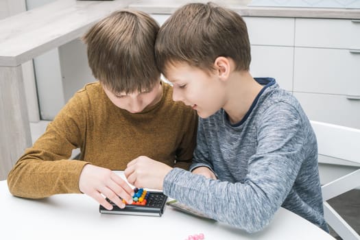 Happy schoolboys play toy constructor sitting at table. Children collect colored details on playing board. Hands of players building figure from pieces on board. Educational interesting board game.