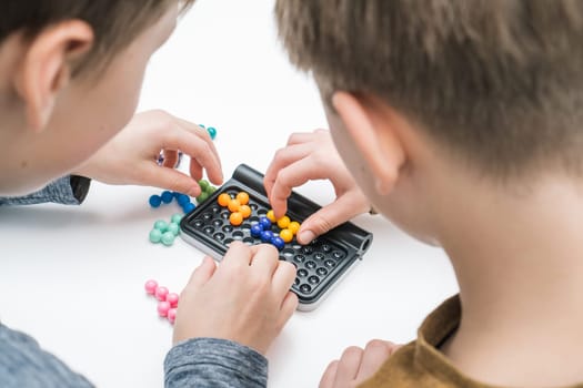 Boys play table tetris on table, from nape view. Children collect colored details on playing board. Hands of players placing figures on board closeup. Educational interesting board game.