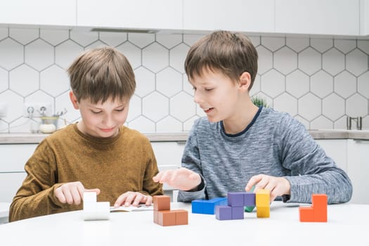 Happy schoolboys play toy constructor sitting at kitchen table. Children collect colored details of lego. Smiling kids fold tetris figures. Friends relax at home. Educational interesting board game.