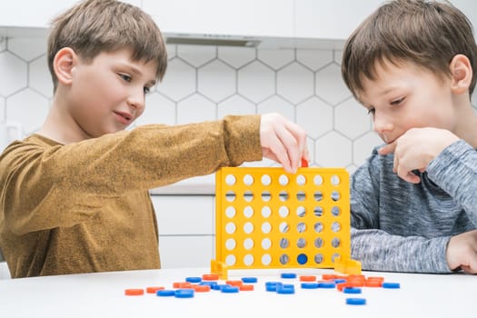 Cute schoolboys play toy constructor sitting at kitchen table. Children collect plastic colored details of lego. Friends relax at home, playtime. Educational interesting board game.