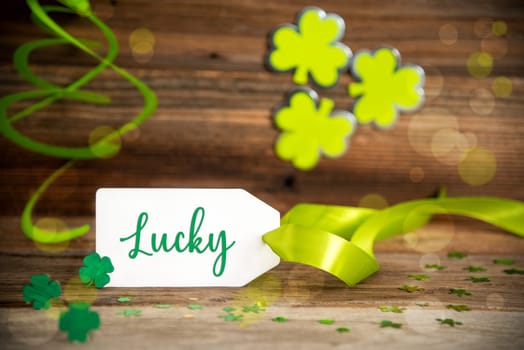 White Label With English Text Lucky. Saint Patrick's Day Decoration With Green Shamrock And Clover. Wooden Vintage Background With Festive Ribbon.
