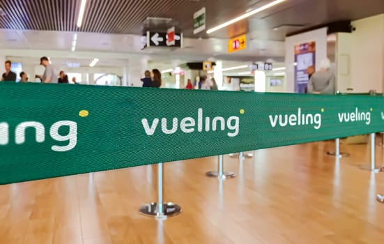 Madrid, SP, Jan 2023: Green belt barrier with white Vueling airlines logo. Vueling is a Spanish low cost airline. Travel and airport security