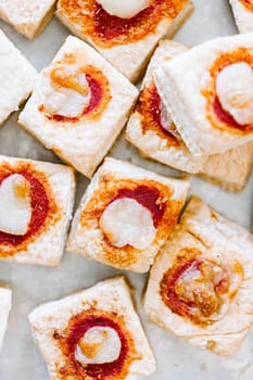 Mini pizzas with mozzarella cheese and fresh basil on a on white baking paper, close-up, top view.Vertical orientation.