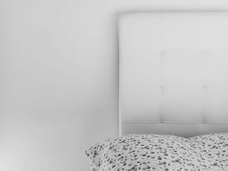Soft headboard. Upholstery for furniture made of genuine or artificial leather and quilted fabric. Soft headboard against a light wall. Black and white monochrome photo.
