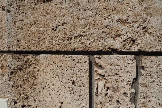 Textured wall lined with beige shell rock tiles. Close-up of a wall made of ancient shell rock. Holes, irregularities of natural building material. Church wall in Banja Koviljaca, Serbia.