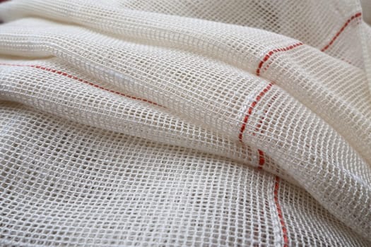 White coarse cotton or linen curtains made of weaves of thin threads. Simple compact economical apartment interior. Window decoration in the room. Red stripe. The fabric is folded in soft waves.