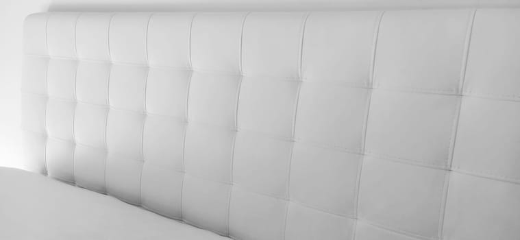 Soft headboard. Upholstery for furniture made of genuine or artificial leather and quilted fabric. Soft headboard against a light wall. Black and white monochrome photo.