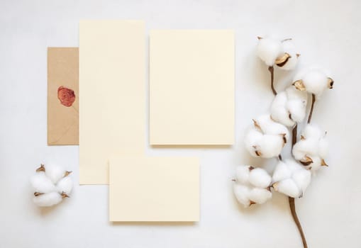 Blank cards and envelope with cotton flowers top view on white, mockup. Romantic scene with wedding suite. Bohemian pastel greeting or wedding set