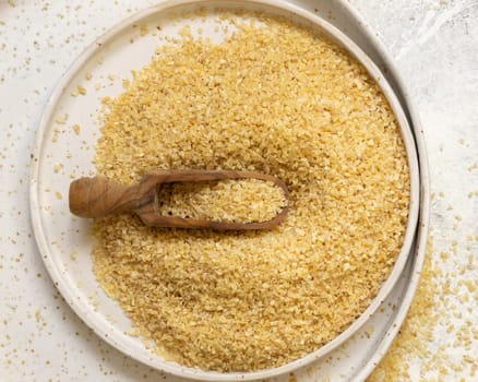Pile of Dry uncooked bulgur wheat grain with a scoop on a plate top view. Vegetarian and Vegan, Mediterranean and Middle Eastern cuisine. Healthy lifestyle
