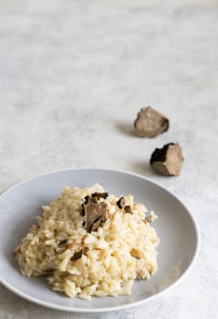Risotto with wild porcini mushrooms and black truffles from Italy served in a plate close up on white table, copy space. Eating Italian gourmet cousine