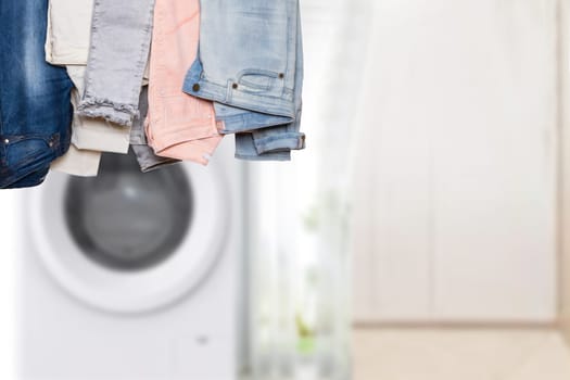 Hanging collection of female various denim pants or colorful trousers in front of abstract blurred bath background with copy space. For your product display montage.