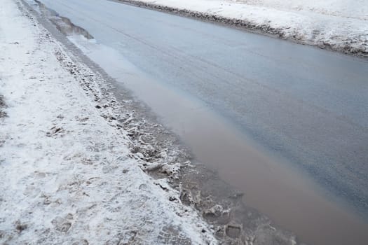 Ice on city roads. Wet asphalt with sand. Snow-covered roadsides. Weather forecast. Thaw in winter. Snow melting. The air temperature is near zero. Footprints of people. Difficult driving conditions