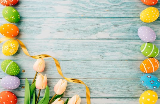 Happy Easter Day Concept. Flat lay holiday banner background web design white colorful easter eggs painted with tulips flowers on blue wood background with empty copy space, overhead, template