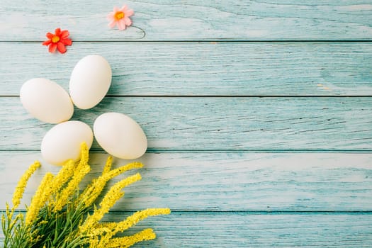 Happy Easter Day Concept. Top view of holiday banner background design white easter eggs and spring yellow flowers on blue wooden background with empty copy space, celebration greeting card